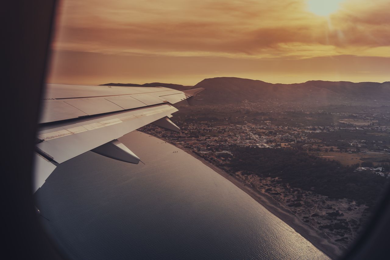 Scenic sunset view of coastline and ocean from airplane window, capturing travel essence.