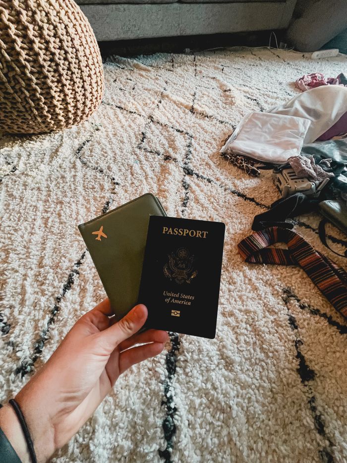 Hand holding two passports on a patterned carpet indoors, travel essentials.